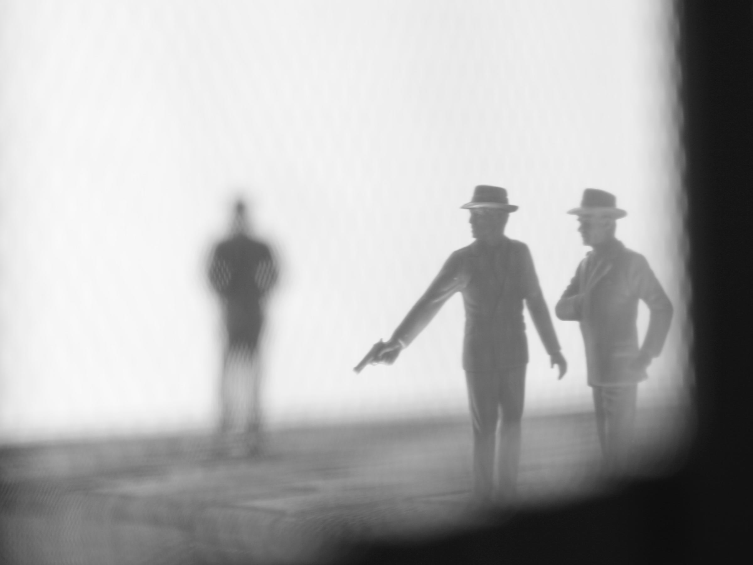 Three hazy monochrome figures seen through a translucent surface